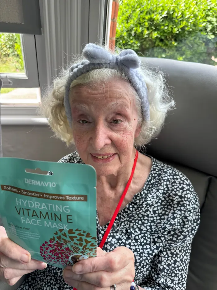 A resident in a headband holding up a face mask on a pamper day