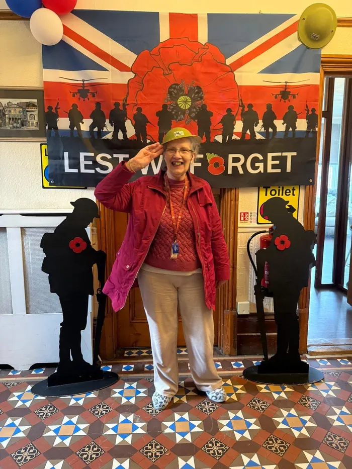 A resident saluting in front of a Lest We Forget display